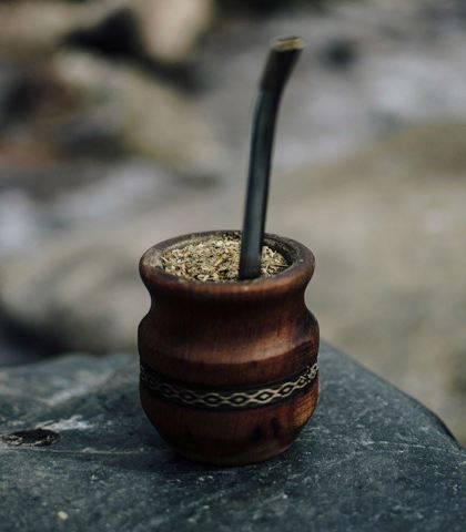 Drewniane naczynie z metalową bombillą wypełnione zmieloną yerba mate, umieszczone na kamieniu.
