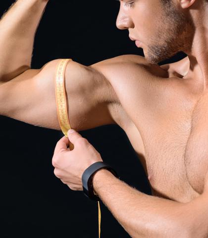 Młody mężczyzna mierzy obwód swojego bicepsa.