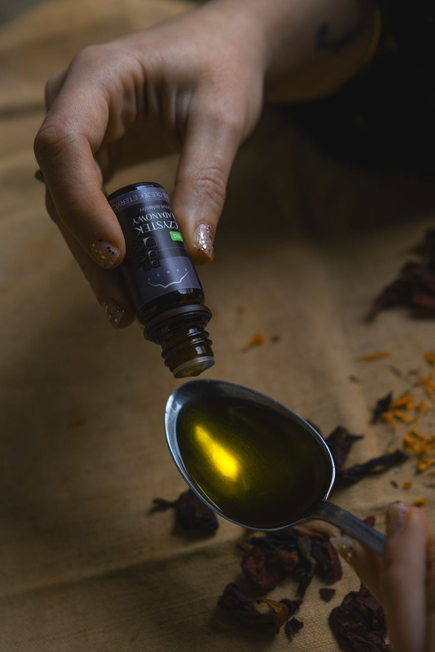 dłonie trzymają olejek eteryczny i dodają go na łyżkę z olejem bazowym