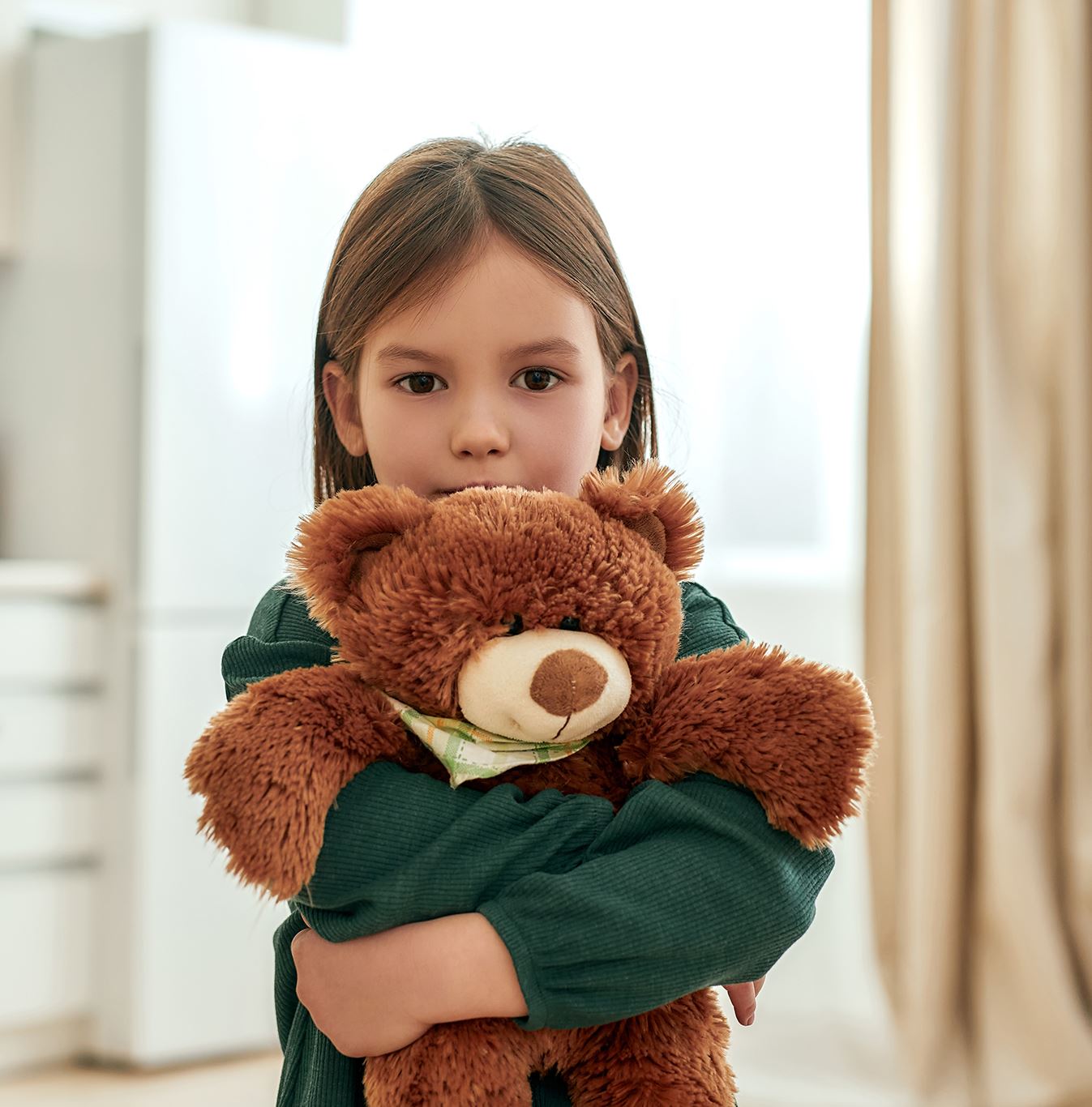 Dziewczynka w wieku szkolnym obejmuje pluszowego, brązowego misia.
