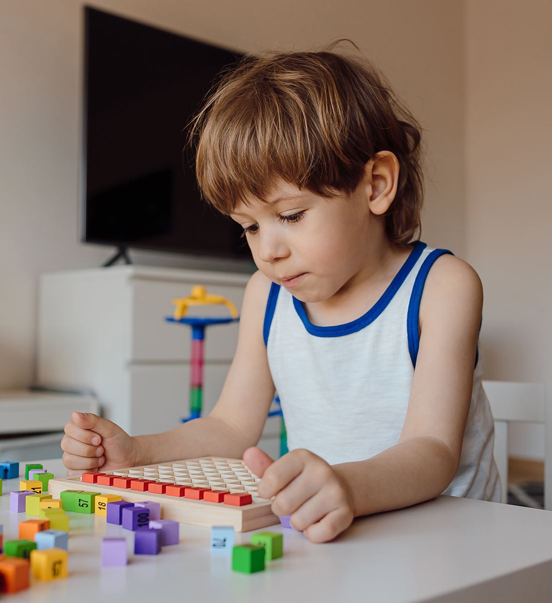 Kilkuletni, skupiony chłopiec układa przy biurku kolorowe klocki.