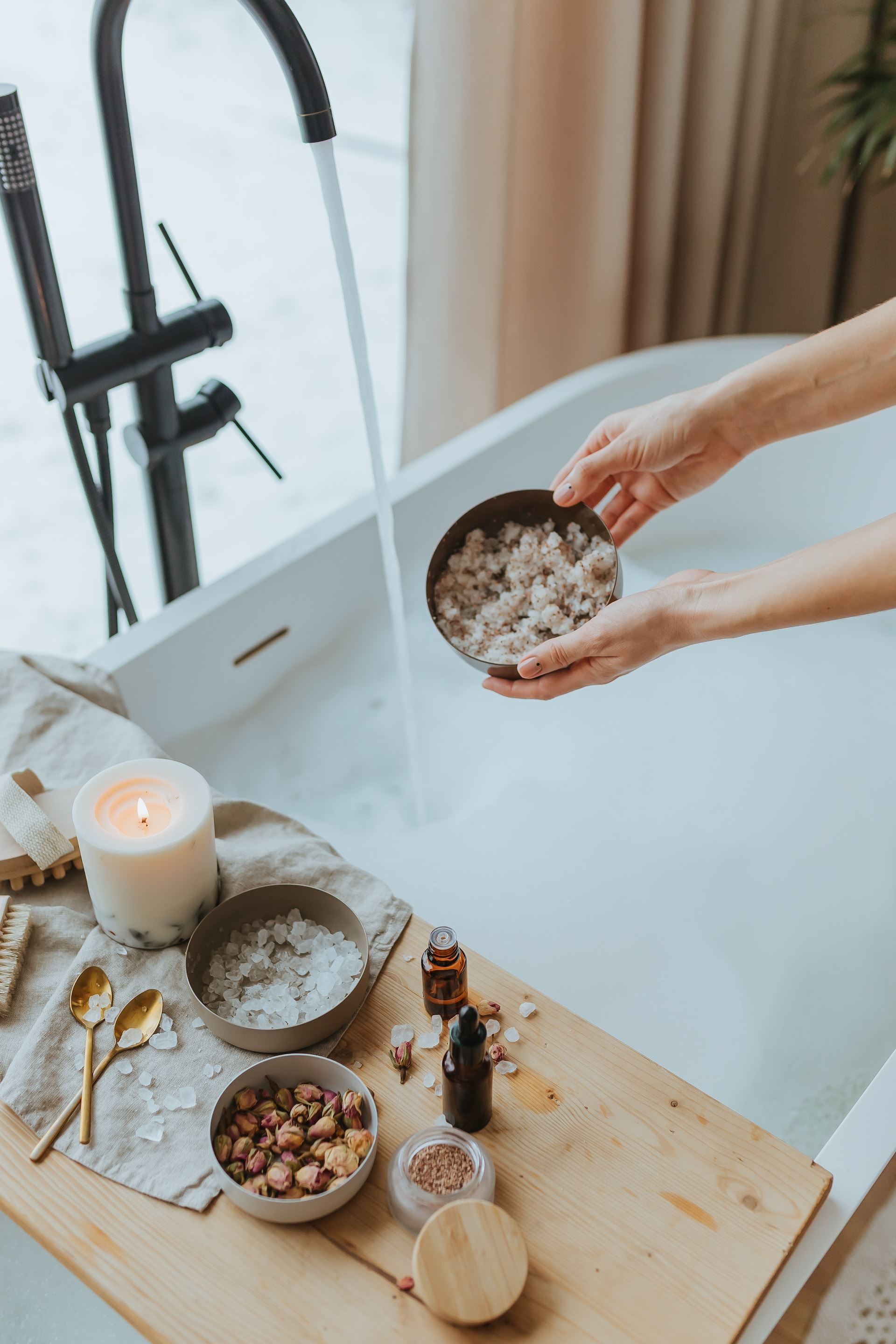 Wanna napełniona wodą, sole, płatki kwiatów i świeczka - przygotowanie relaksującej kąpieli